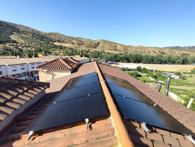 Paneles solares negros sobre tejado de teja, con la sierra al fondo